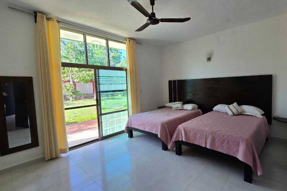 A hotel room with two beds, a ceiling fan, and a large sliding glass door leading to a balcony.