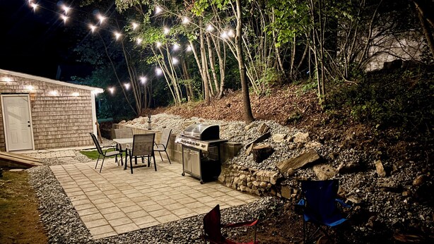 Une terrasse extérieure avec un barbecue, des chaises et des guirlandes lumineuses.