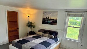 Une chambre à coucher avec un lit, une table de chevet, une lampe, une fenêtre et une porte.