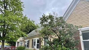 Une maison d’habitation avec un jardin devant, un banc et un arbre.