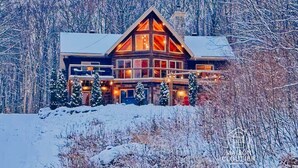A large, multi-story log cabin with a prominent gabled roof, surrounded by snow-covered trees.