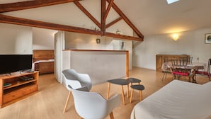 A loft-style room with exposed wooden beams, a television, a sofa, a dining table with chairs, and a skylight. - Holiday Home 'Maison' with Mountain View and Wi-Fi (Noyarey)