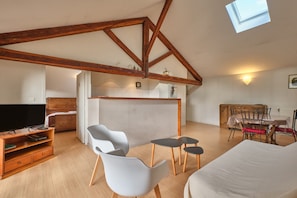 Una stanza in stile loft con travi a vista in legno, una televisione, un divano, un tavolo da pranzo con sedie e un lucernario.