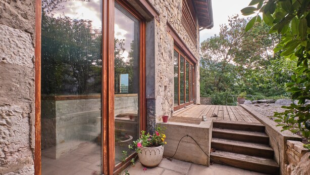 A stone building with large glass doors, a wooden deck, and a potted plant. - Holiday Home 'Maison' with Mountain View and Wi-Fi (Noyarey)