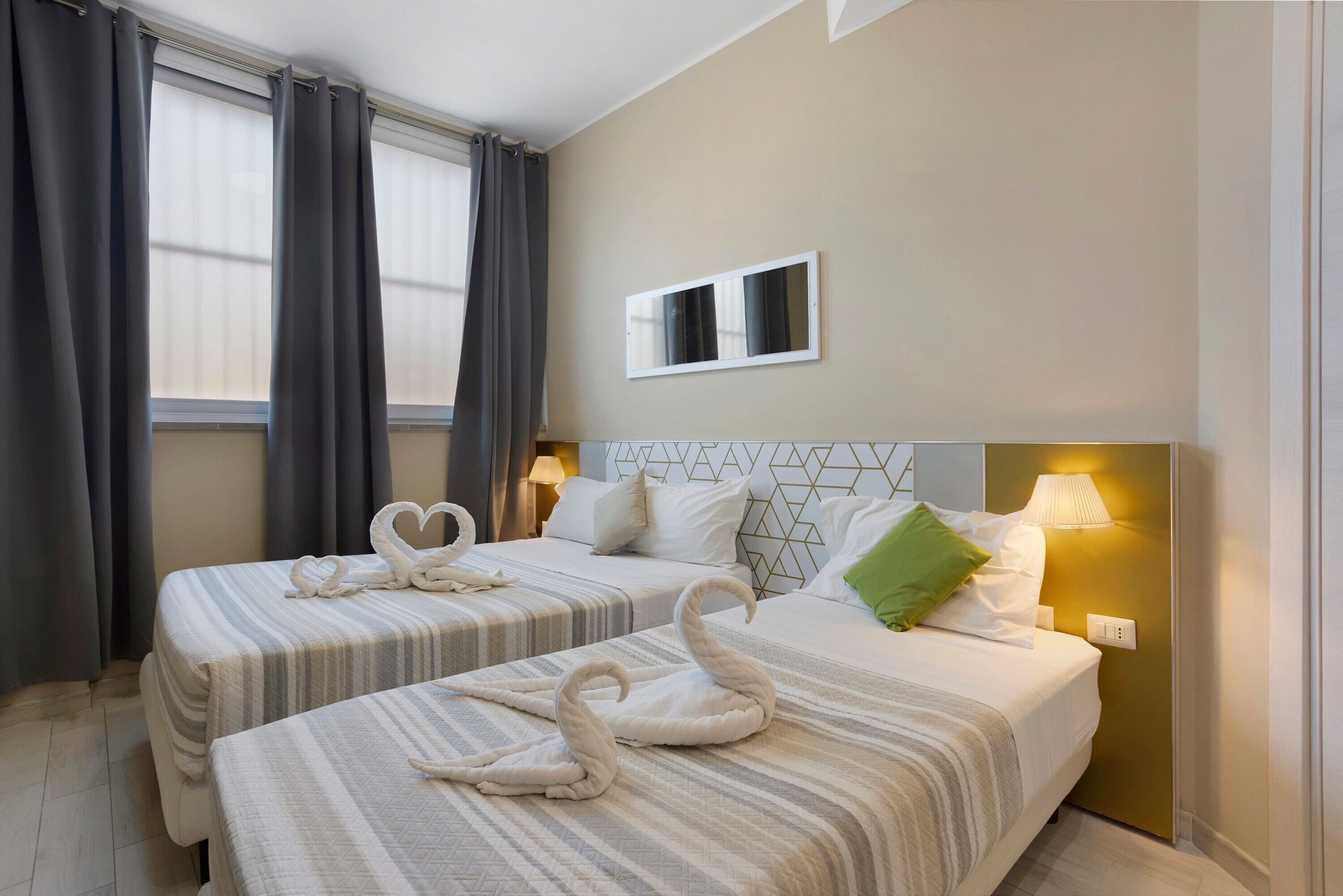 A hotel room with two beds, a mirror, and a wall-mounted lamp.