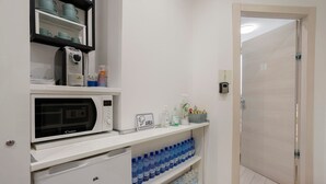 A kitchenette with a microwave, a coffee maker, and a shelf with water bottles. - Room 'Tripla' with Wi-Fi and Air Conditioning (Milano)