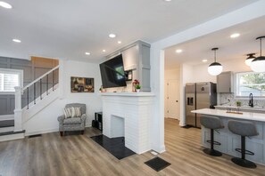 A modern kitchen with a white brick fireplace, stainless steel appliances, and a bar area with stools.