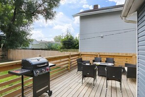 A deck with a grill, outdoor furniture, and a wooden fence.