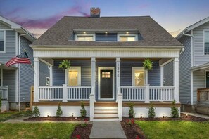 Ein zweistöckiges Haus mit einer Veranda, einer schwarzen Haustür und einer amerikanischen Flagge.