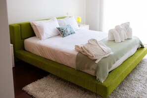 Un lit à baldaquin vert avec une literie blanche, un tapis blanc moelleux et une lampe sur une table de chevet.