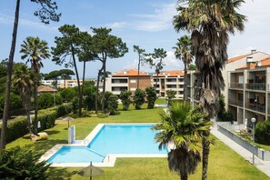 A swimming pool surrounded by greenery, with a view of multi-story buildings in the background. - Apartment 'Fão' with Shared Pool, Shared Garden and Wi-Fi (Fão)