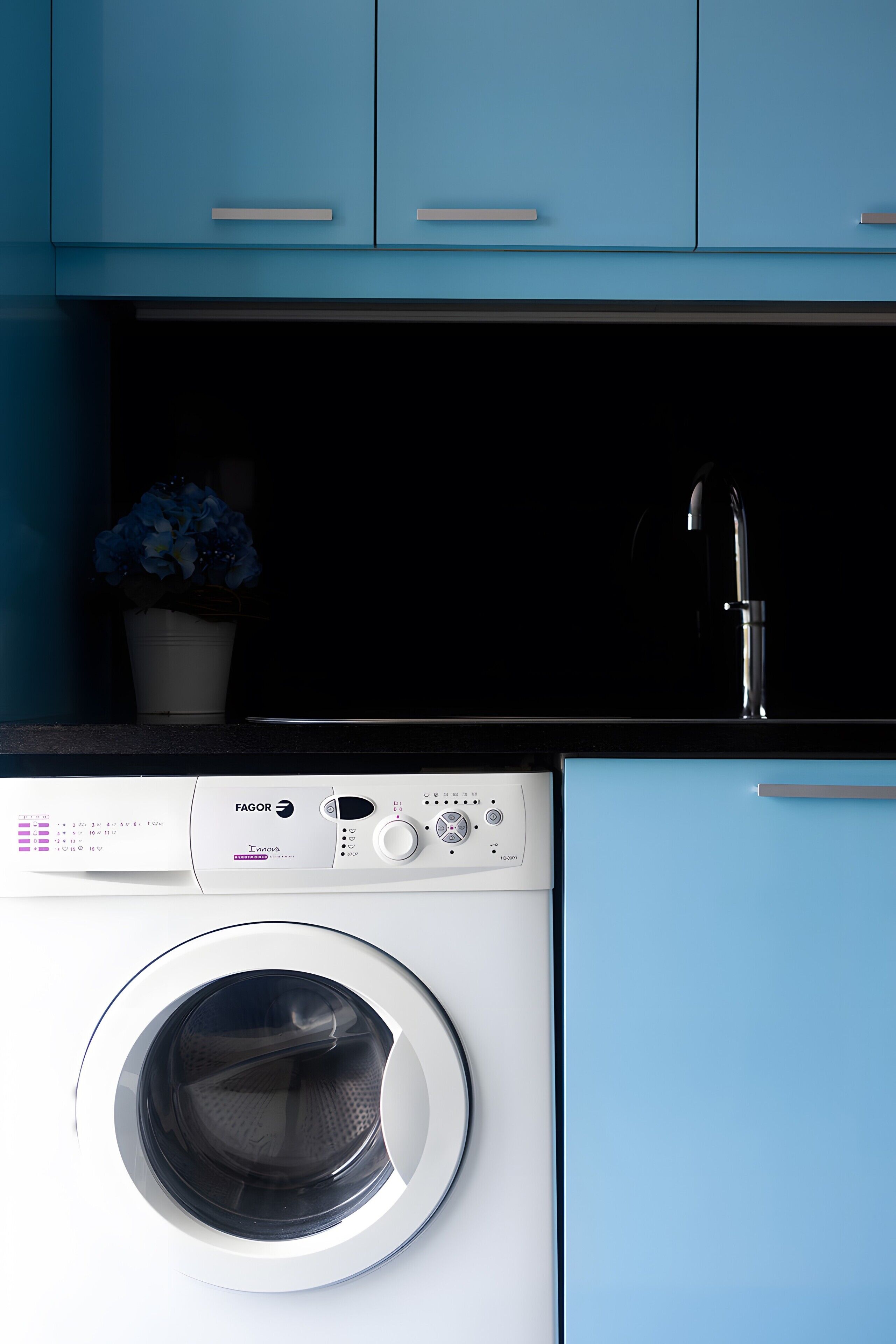Een wasmachine met voorlaadklep, een bedieningspaneel, een wastafel en een potplant.