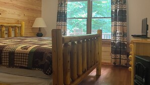Ein Bett mit Holzrahmen, einer Bettdecke, einer Nachttischlampe und einem Fenster mit Vorhängen.
