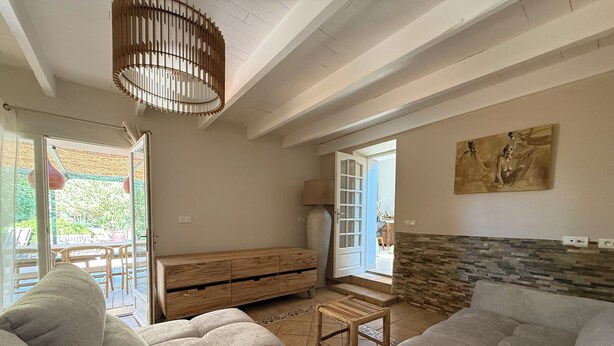 Ein geräumiges Wohnzimmer mit einer großen Couch, einer hölzernen Bank und einem kleinen Tisch. Eine Tür führt zu einem Außenbereich mit einer Terrasse.