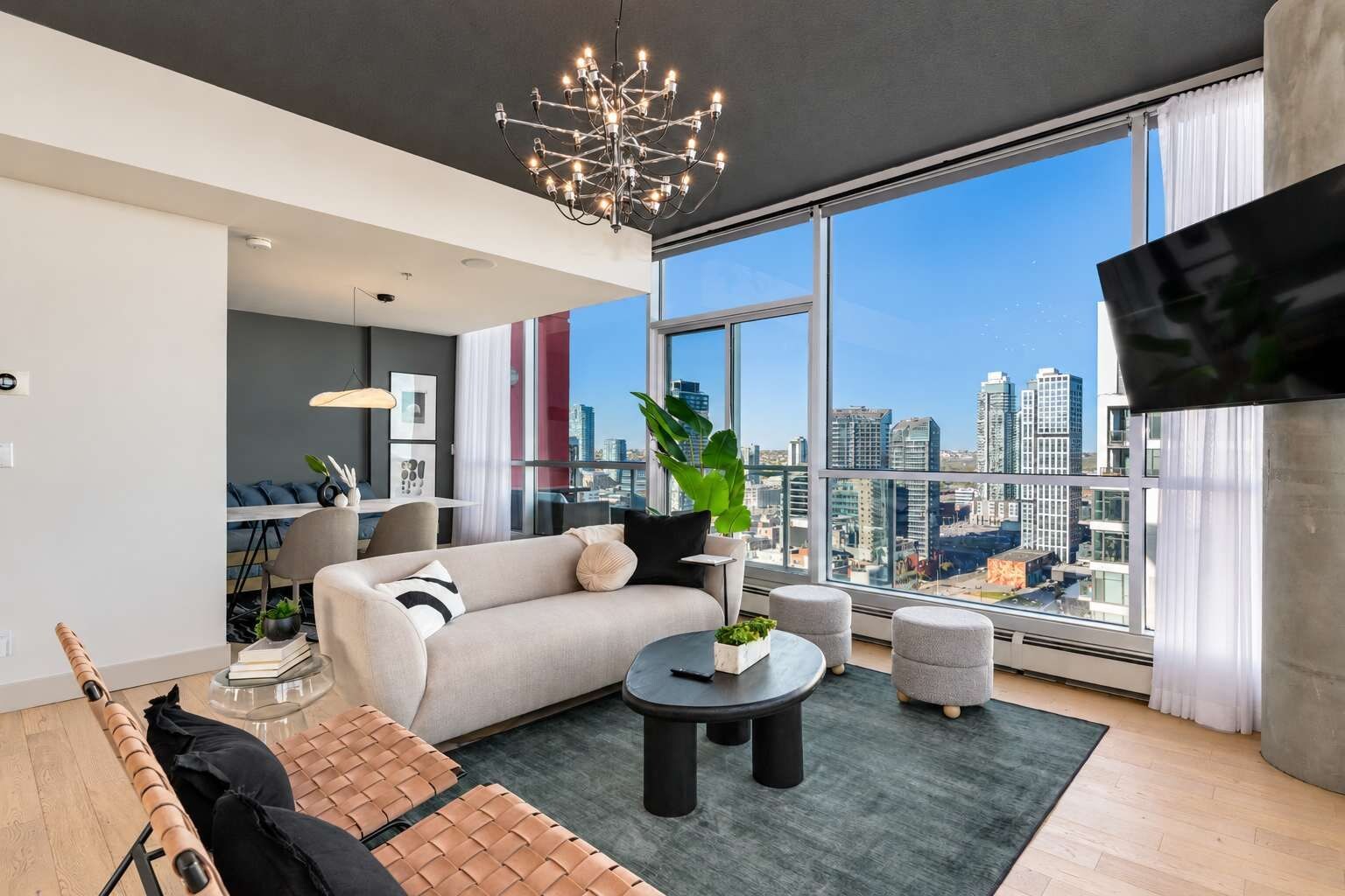 A modern living room with a sofa, coffee table, and a view of a cityscape through large windows.