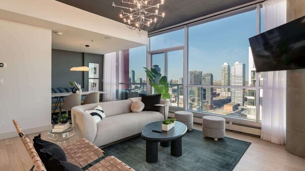 A modern living room with a large window, a sofa, a coffee table, and a TV. - 2-Storey PH Pano Views+2 Terraces|Parking|Soaker Tub (Calgary)