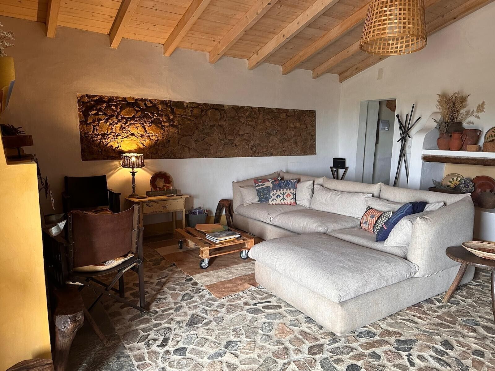A cozy living room with a stone floor, a sofa, a chair, a lamp, and a wall art piece.