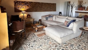 A cozy living room with a stone floor, a sofa, a chair, a lamp, and a wall art piece. - Holiday Home 'Herdade Da Carapuça' with Mountain View, Private Pool and Wi-Fi (Portalegre)