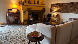 A cozy living room with a stone floor, a sofa, a table with a lamp, and a fireplace. - Holiday Home 'Herdade Da Carapuça' with Mountain View, Private Pool and Wi-Fi (Portalegre)