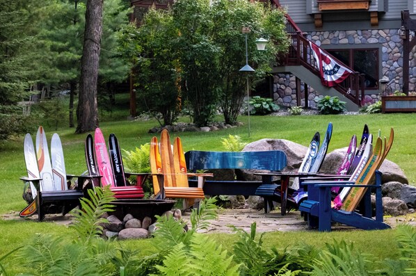 A row of colorful kayaks and paddleboards in a garden setting with a stone house and stairs in the background. - Timberhaus on Garfield Lake (Laporte)
