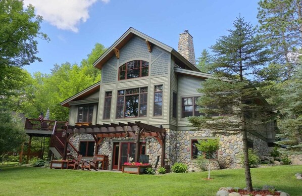 A two-story house with a stone facade, large windows, and a wooden deck with outdoor furniture.