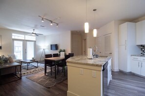 A modern kitchen with a central island, a dining area with a table and chairs, and a living room with a sofa and a TV.