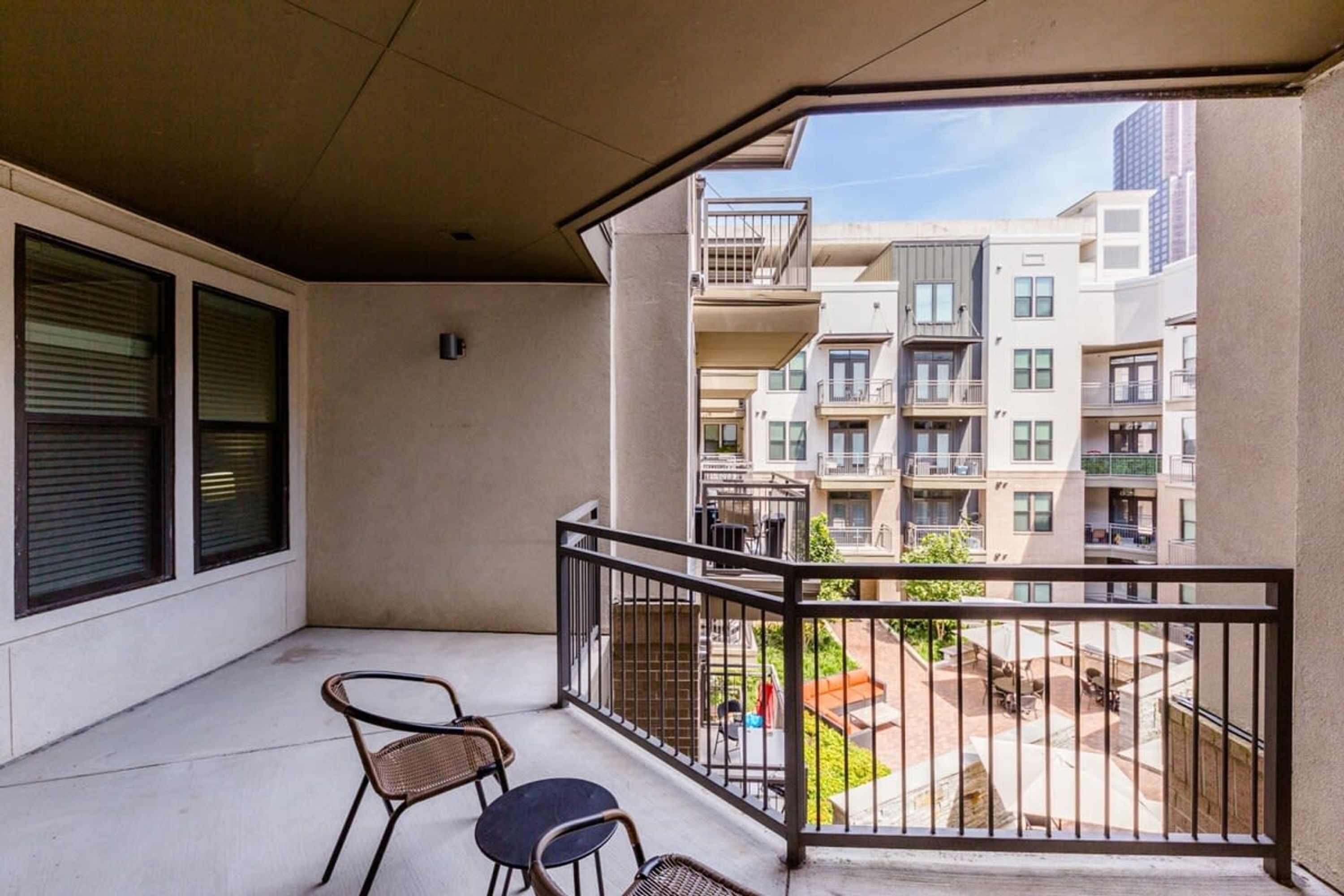 A balcony with two chairs, a view of neighboring apartment buildings, and a clear sky.