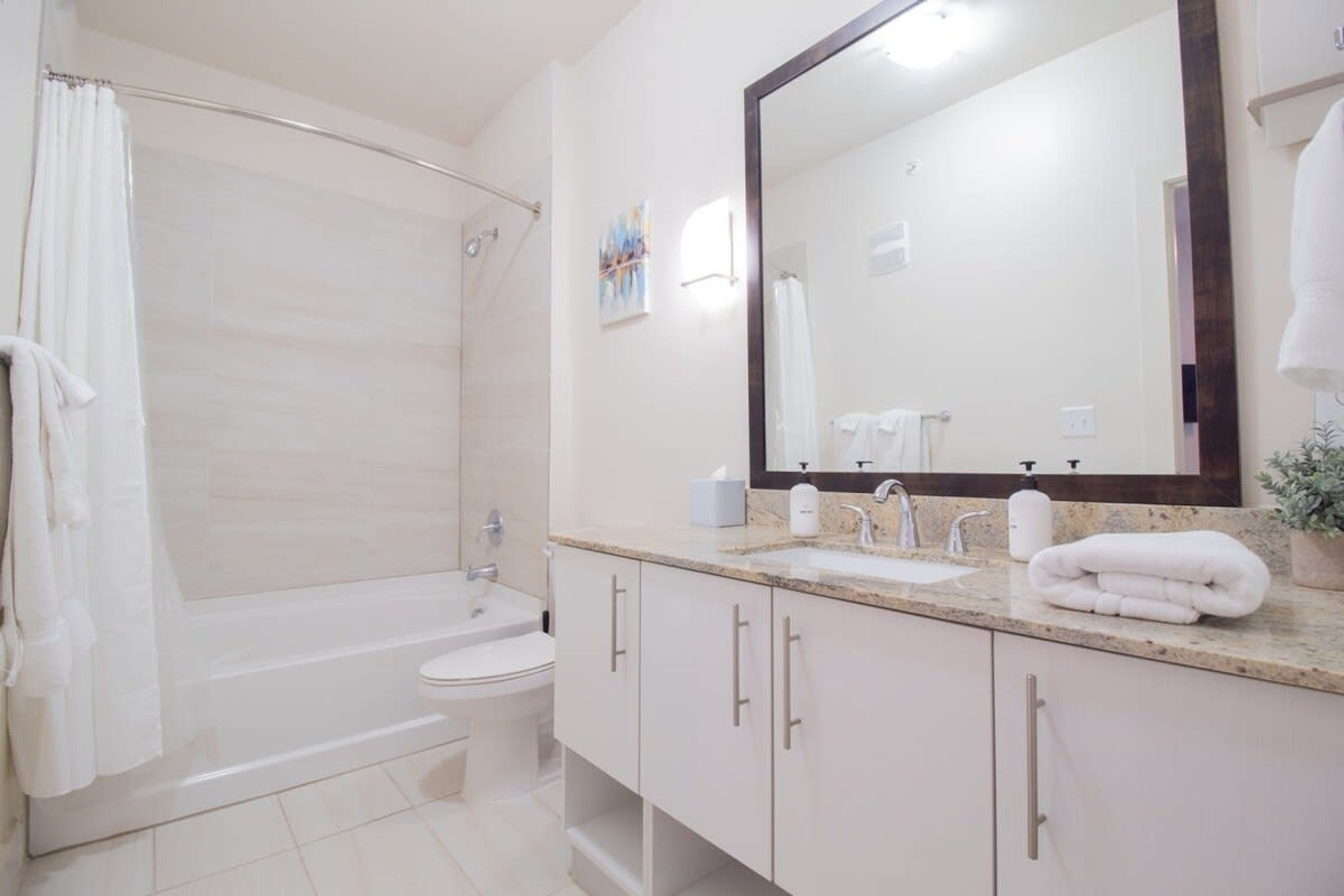 Ein modernes Badezimmer mit Badewanne, Toilette, Waschbecken und großem Spiegel.