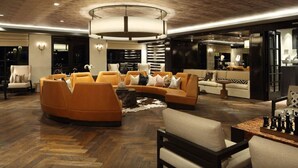 A spacious living room with a large, curved orange sofa set, a wooden herringbone floor, and a central chandelier. - Revive Tanglewood Stunning 2BR in Uptown Houston (Houston)