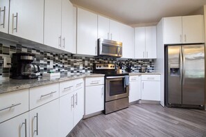 A modern kitchen with white cabinets, a stainless steel refrigerator, a microwave, and a coffee maker.