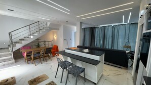 A modern kitchen with a central island, a dining area with a wooden table and chairs, and a staircase leading to an upper level. - Villa with swimming pool 7mn from port Say (Marsa Ben M'Hidi)