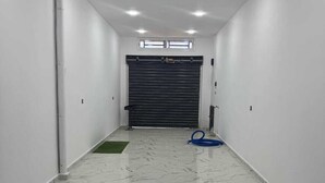 A hallway with white walls, a marble floor, and a closed black roller door at the end. - Villa with swimming pool 7mn from port Say (Marsa Ben M'Hidi)
