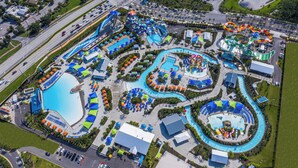 Vista aérea de un parque acuático con varias piscinas, toboganes y una gran piscina central rodeada de sombrillas y áreas de descanso.