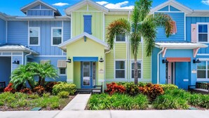 Una hilera de casas urbanas coloridas con una entrada central, rodeadas de jardines bien cuidados.