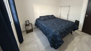 A bedroom with a bed, an air conditioning unit, a small bedside table with a picture frame and remote control, and a door. - House for 8 with Private Pool (San Carlos)
