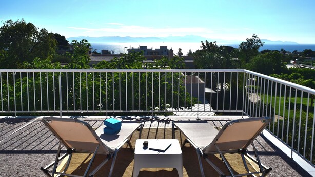A balcony with two chairs and a table, overlooking a scenic view of the sea and mountains. - Stunning Seaview Apartment (Nea Makri)