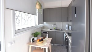 A compact kitchen with grey cabinets, a sink, and a coffee maker. A small table with a bowl of fruit and a plant is visible. - Stunning Seaview Apartment (Nea Makri)
