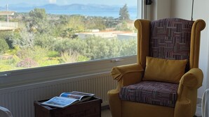 A yellow armchair with a patterned cushion in front of a window with a view of greenery and distant mountains. - Stunning Seaview Apartment (Nea Makri)