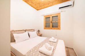 Un dormitorio con techo de madera, una cama con ropa blanca, una ventana con contraventanas de madera y un equipo de aire acondicionado.