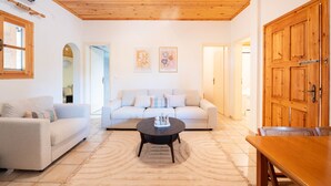A living room with a wooden ceiling, a white sofa, a round coffee table, and a wooden door.