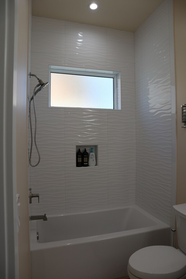 A bathroom with a bathtub, a toilet, and a window above the bathtub.