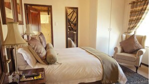 A bedroom with a large bed, a chair, a nightstand, and a mirror. - Luxury 3 Apartment (Sandton)