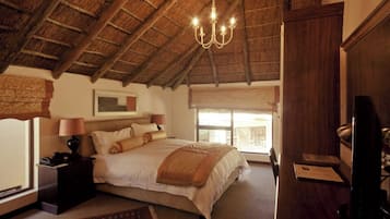 Ein Schlafzimmer mit einem Reetdach, einem Bett mit weißer Bettwäsche, einer Kandelaber und einem Schreibtisch mit Stuhl.