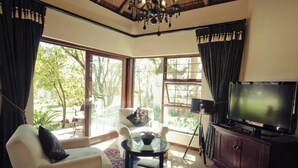 Un salon avec un canapé, une table basse en verre, un téléviseur posé sur un meuble en bois et de grandes fenêtres avec des rideaux.