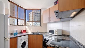 A compact kitchen with a washing machine, microwave, and granite countertop.