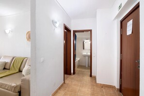 A hallway with a sofa, a wooden door, and a bathroom visible in the background. - Gabriel 5 G Apartment with Sea View, Shared Pool and Wi-Fi (Armação de Pêra)