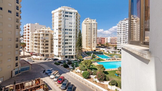 A high-rise residential building with multiple balconies, a swimming pool, and a parking area.