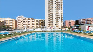 A swimming pool with lounge chairs, surrounded by high-rise buildings.