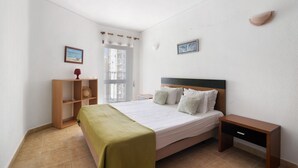 A bedroom with a bed, bedside table, nightstand, and a window with curtains.