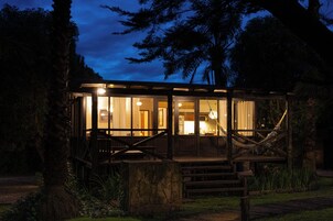 Una baita di legno con fondamenta in pietra, ampie finestre e una scala che conduce all'ingresso.